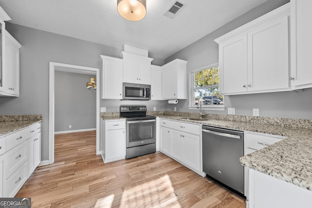 kitchen with stainless steel appliances, light stone countertops, sink, and white cabinets