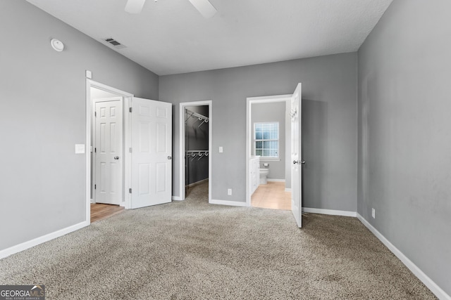 unfurnished bedroom featuring ensuite bath, a walk in closet, ceiling fan, and carpet flooring