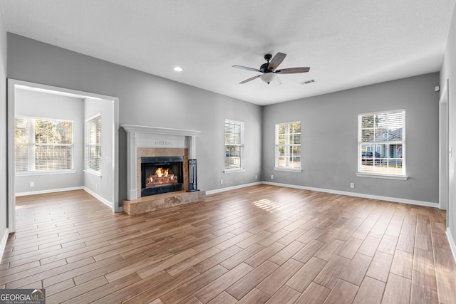 unfurnished living room with ceiling fan, a textured ceiling, a tile fireplace, and a healthy amount of sunlight