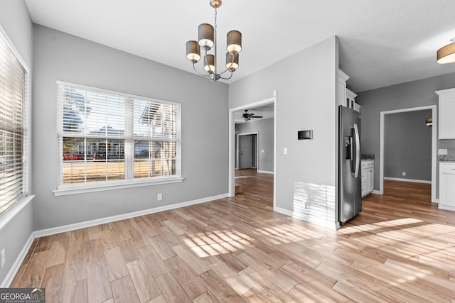 unfurnished dining area with ceiling fan with notable chandelier and light hardwood / wood-style flooring