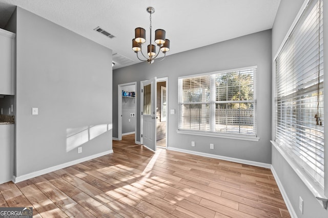 unfurnished dining area with a textured ceiling, light hardwood / wood-style floors, and a chandelier