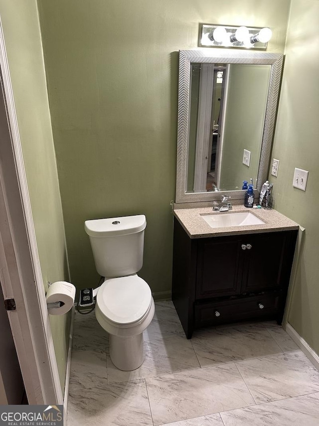 half bathroom with toilet, marble finish floor, baseboards, and vanity