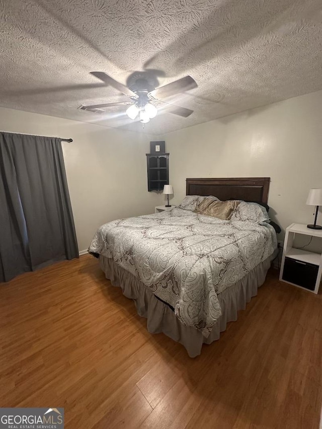 bedroom with ceiling fan, a textured ceiling, and wood finished floors