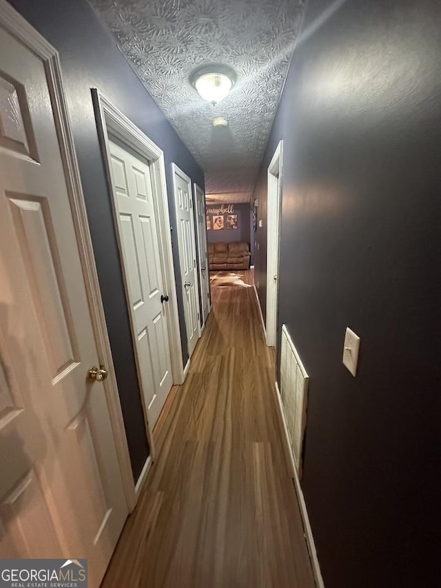 hallway with a textured ceiling, wood finished floors, and visible vents