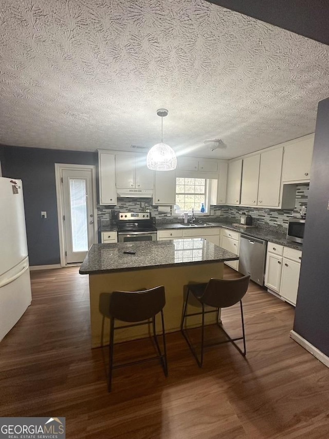 kitchen with dark wood-type flooring, a kitchen bar, hanging light fixtures, stainless steel appliances, and white cabinets