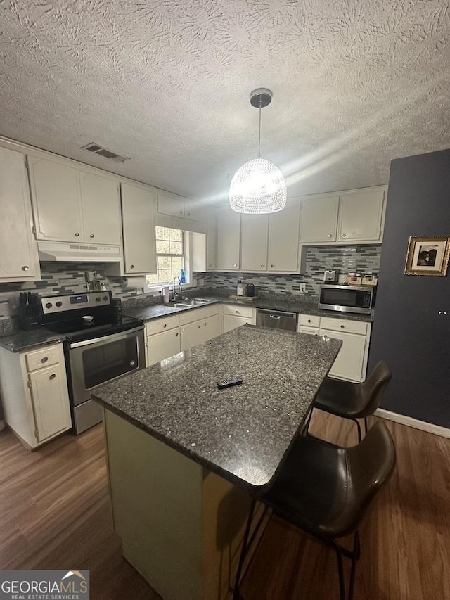 kitchen with stainless steel appliances, dark wood finished floors, a sink, and under cabinet range hood