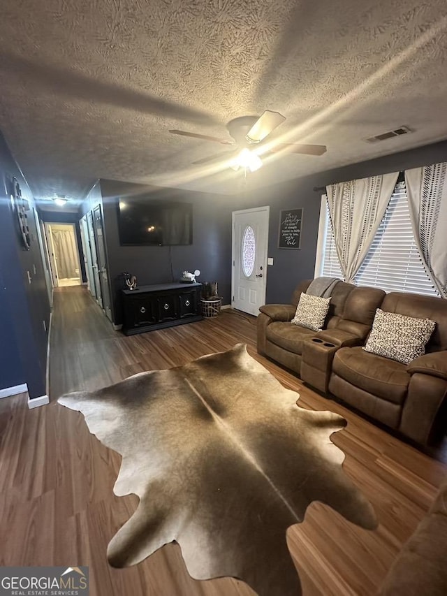 living room featuring visible vents, ceiling fan, a textured ceiling, wood finished floors, and baseboards