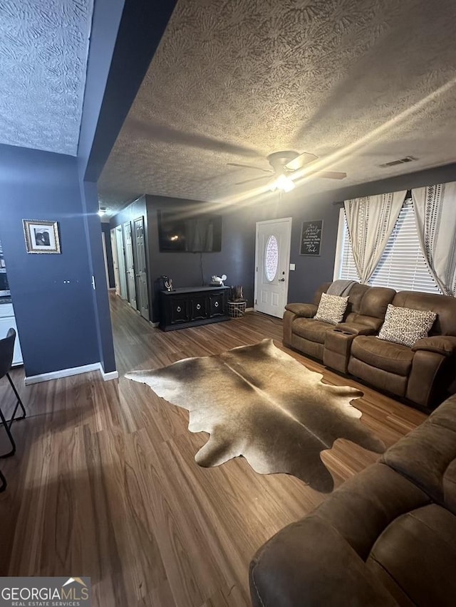 living room featuring a textured ceiling, ceiling fan, wood finished floors, visible vents, and baseboards