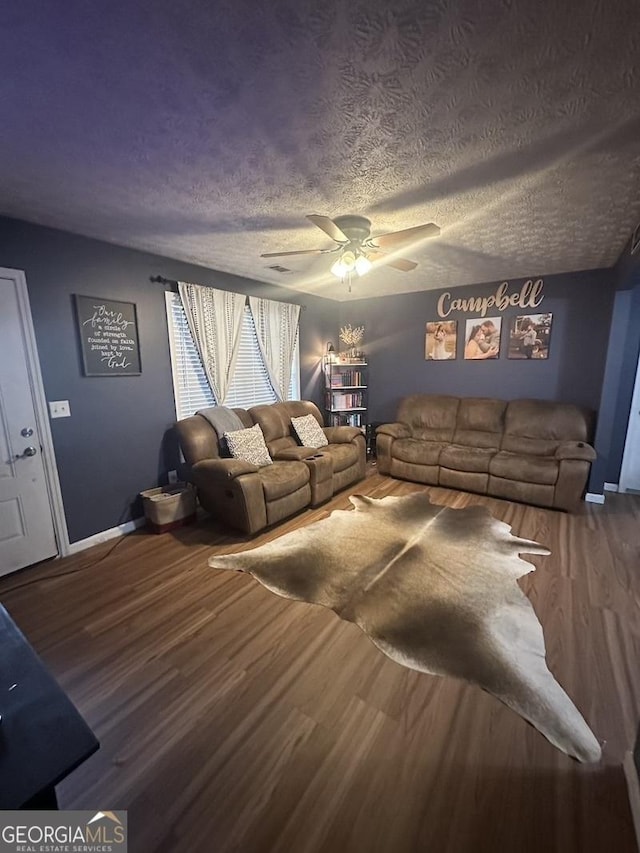 living area with a ceiling fan, a textured ceiling, baseboards, and wood finished floors