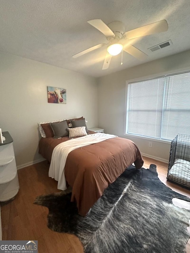 bedroom featuring ceiling fan, a textured ceiling, visible vents, and wood finished floors