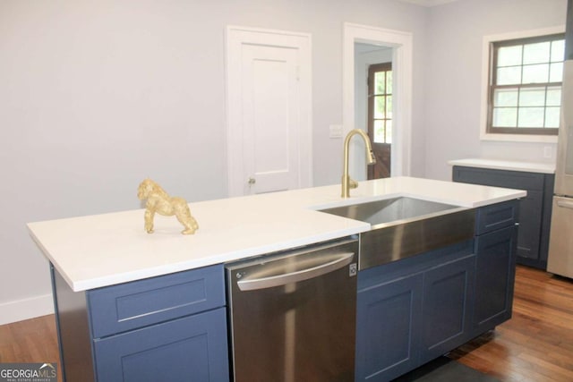 kitchen with dark wood-type flooring, blue cabinetry, sink, stainless steel dishwasher, and an island with sink