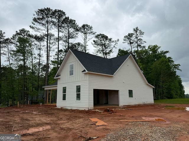 view of side of property with a garage, board and batten siding, a shingled roof, and driveway