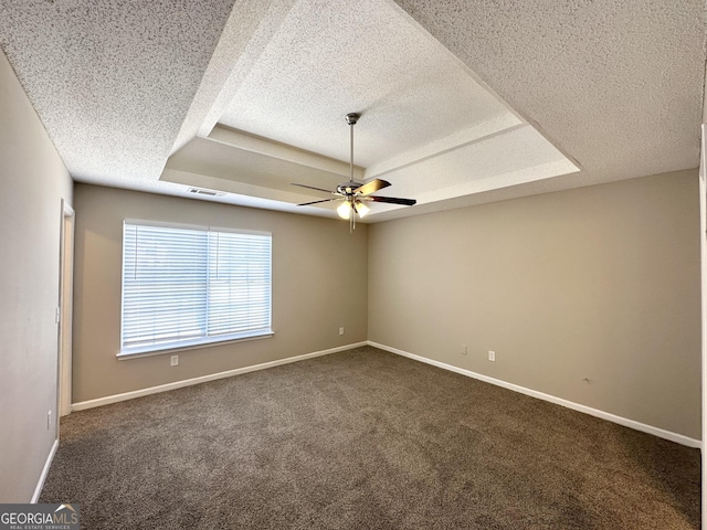 unfurnished room featuring a raised ceiling, a textured ceiling, and dark carpet