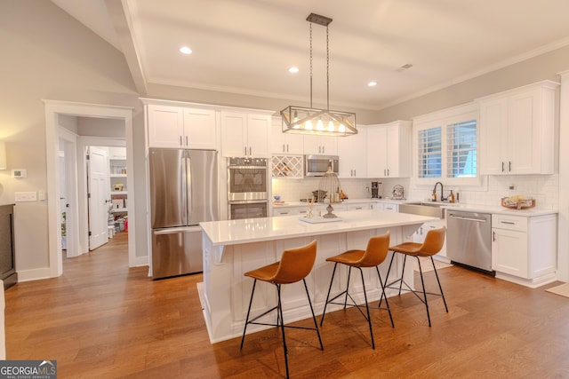 kitchen with sink, appliances with stainless steel finishes, white cabinetry, a kitchen island, and decorative light fixtures