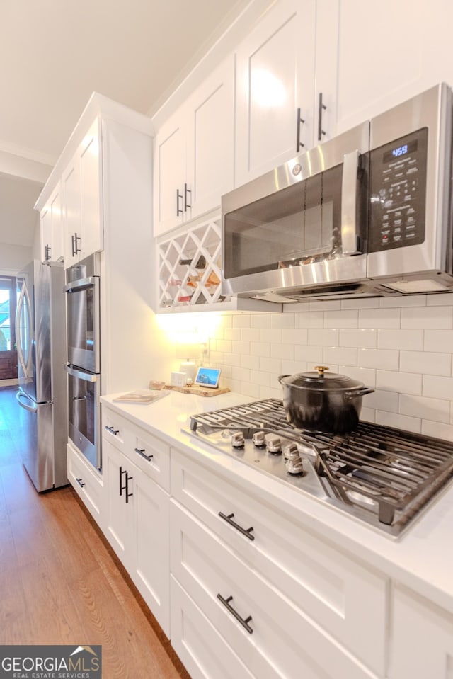 kitchen with white cabinetry, appliances with stainless steel finishes, backsplash, and light wood-type flooring