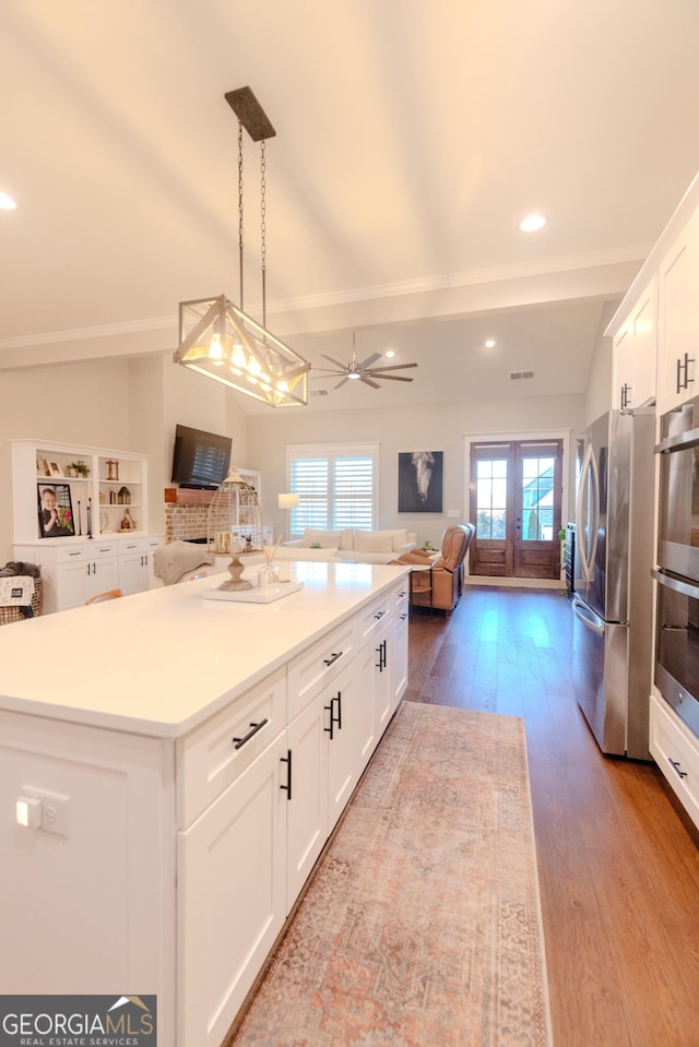 kitchen with decorative light fixtures, stainless steel appliances, a center island, and white cabinets