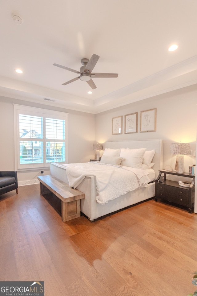 bedroom with a raised ceiling, ceiling fan, and light hardwood / wood-style floors