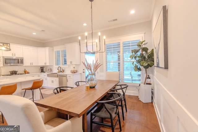 dining space with ornamental molding, sink, an inviting chandelier, and light wood-type flooring