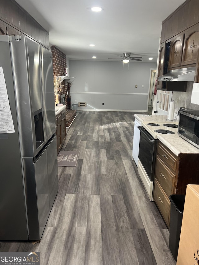 kitchen featuring dark wood-type flooring, dark brown cabinetry, appliances with stainless steel finishes, ceiling fan, and a fireplace