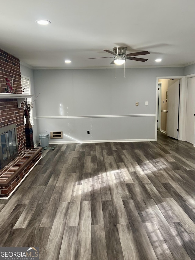 unfurnished living room featuring crown molding, a brick fireplace, dark wood-type flooring, and ceiling fan