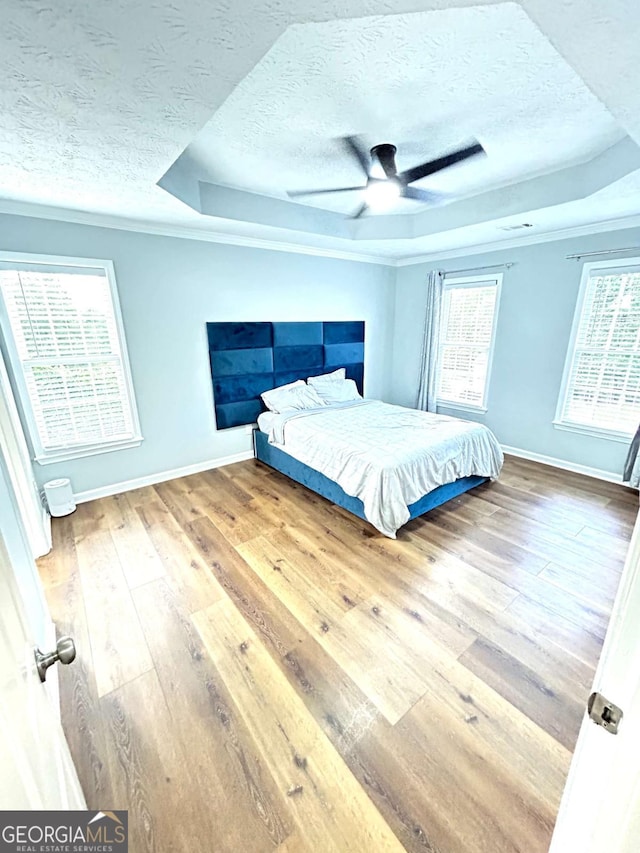 bedroom featuring a raised ceiling, wood-type flooring, a textured ceiling, and ceiling fan