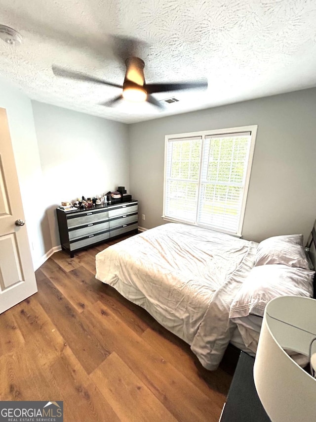 bedroom with a textured ceiling, dark wood-type flooring, and ceiling fan