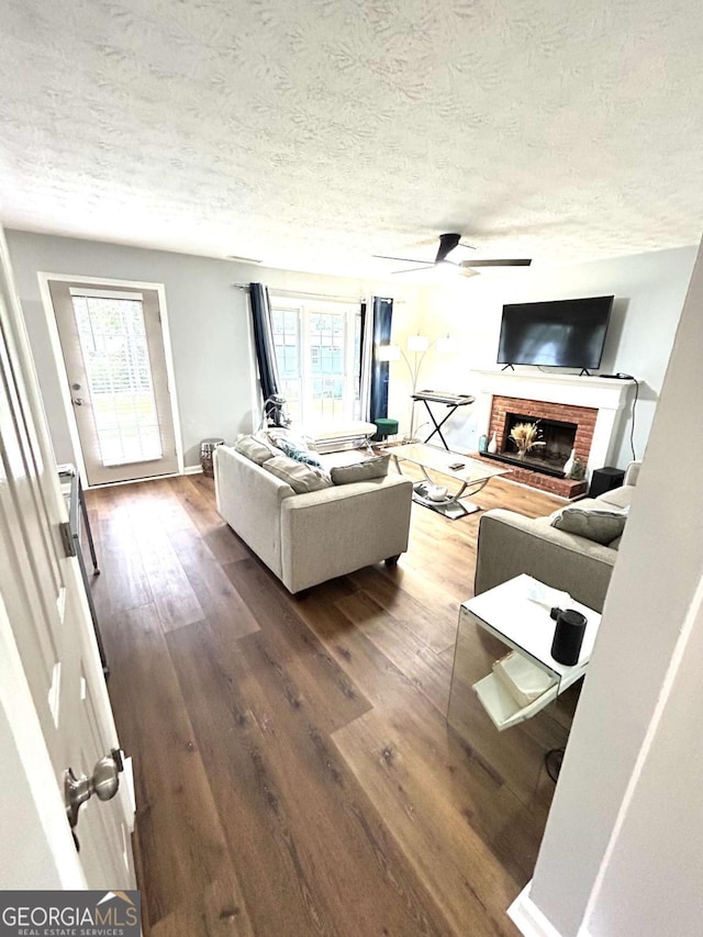 living room featuring wood-type flooring, a brick fireplace, ceiling fan, and a textured ceiling