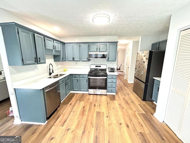 kitchen featuring appliances with stainless steel finishes, light hardwood / wood-style floors, sink, and a textured ceiling