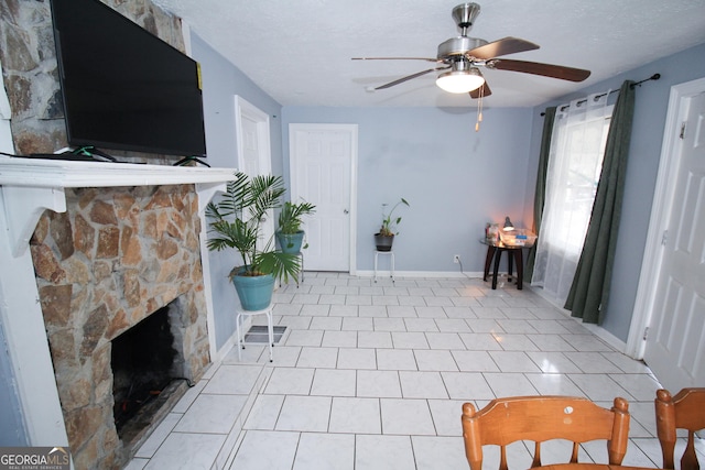 tiled entryway with ceiling fan, a stone fireplace, and a textured ceiling