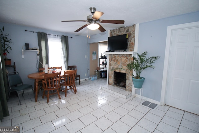 tiled dining space featuring ceiling fan and a stone fireplace