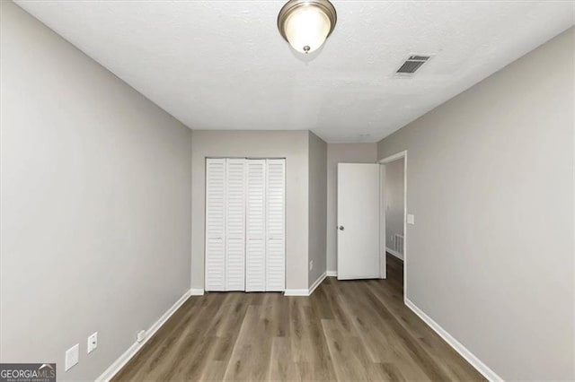 unfurnished bedroom with wood-type flooring, a closet, and a textured ceiling