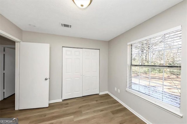 unfurnished bedroom featuring multiple windows, wood-type flooring, and a closet