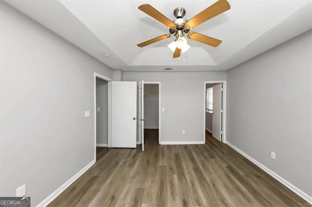 unfurnished bedroom with a raised ceiling, dark wood-type flooring, and ceiling fan