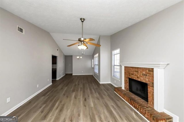 unfurnished living room with lofted ceiling, a brick fireplace, a textured ceiling, dark hardwood / wood-style floors, and ceiling fan with notable chandelier