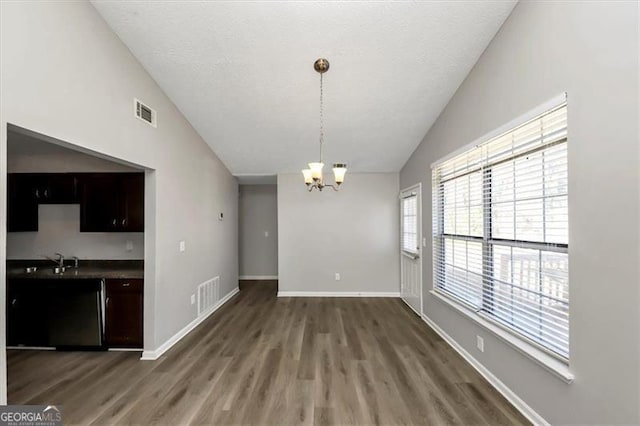 unfurnished dining area featuring an inviting chandelier, sink, vaulted ceiling, and dark hardwood / wood-style floors