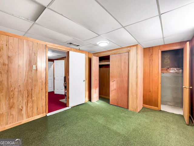 unfurnished bedroom with a drop ceiling, wooden walls, and a closet