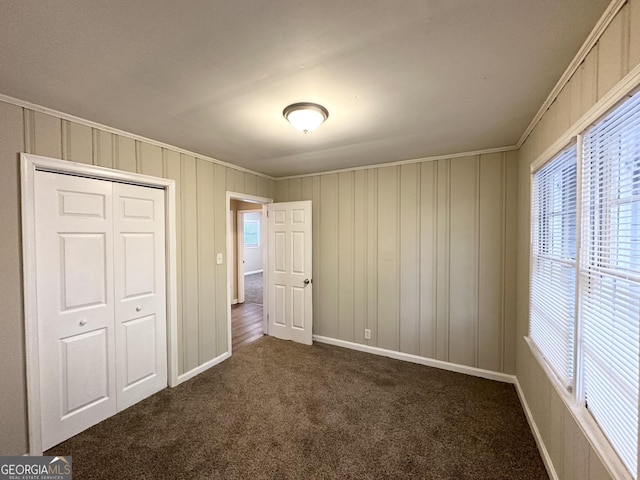 unfurnished bedroom with crown molding, dark carpet, and a closet