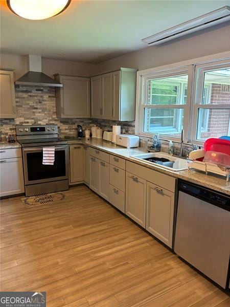 kitchen featuring sink, light hardwood / wood-style flooring, stainless steel appliances, tasteful backsplash, and wall chimney exhaust hood