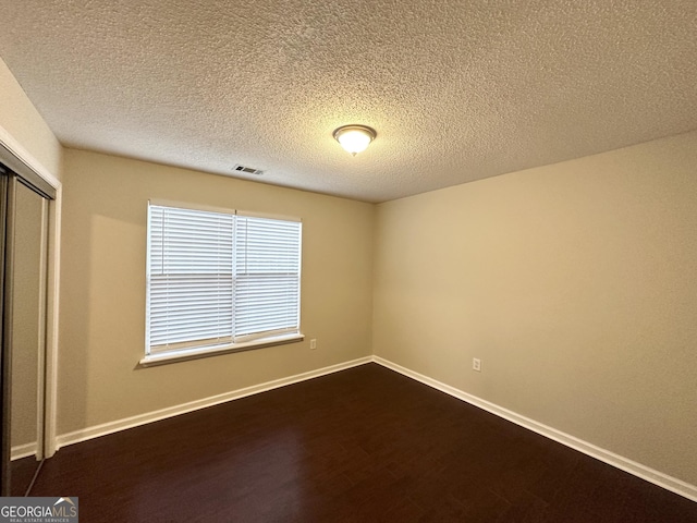 spare room featuring dark hardwood / wood-style flooring and a textured ceiling