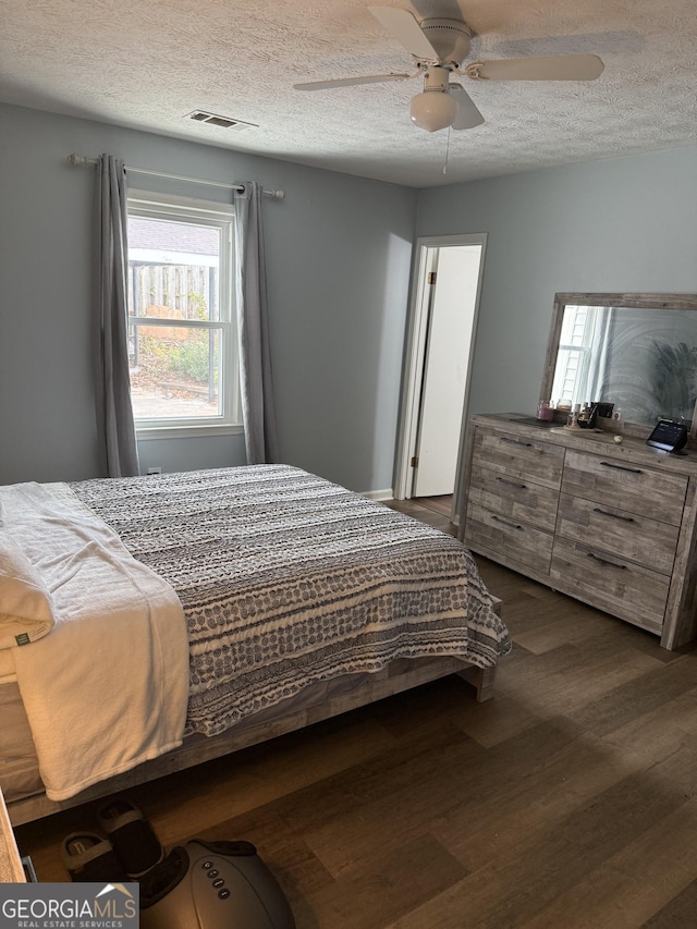 bedroom with a textured ceiling, dark wood-type flooring, and ceiling fan