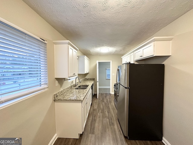 kitchen featuring sink, dark wood-type flooring, stainless steel refrigerator, white cabinetry, and light stone counters