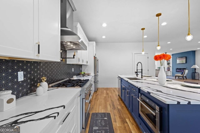 kitchen with wall chimney range hood, blue cabinetry, appliances with stainless steel finishes, white cabinetry, and decorative light fixtures