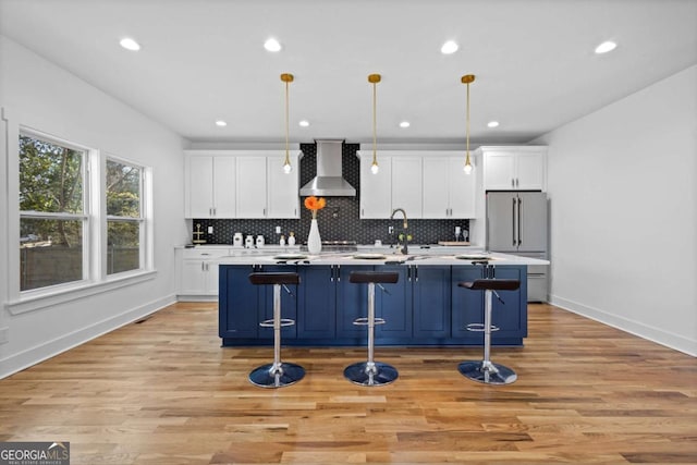 kitchen featuring an island with sink, a breakfast bar area, hanging light fixtures, light hardwood / wood-style floors, and wall chimney range hood