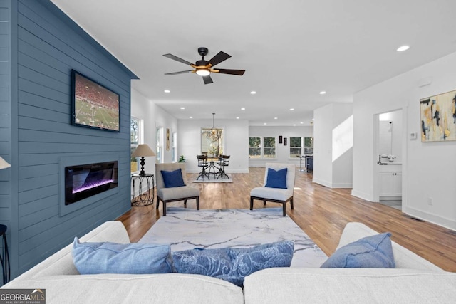 living room featuring ceiling fan, a large fireplace, and light hardwood / wood-style flooring