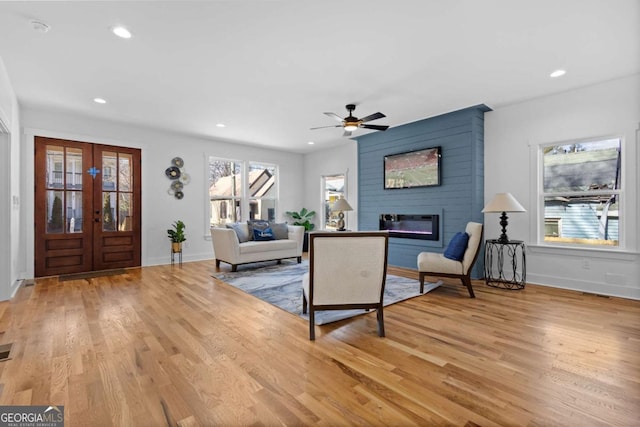 living room featuring french doors, a large fireplace, ceiling fan, and light hardwood / wood-style flooring