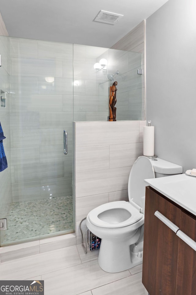 bathroom featuring vanity, toilet, a shower with door, and tile walls