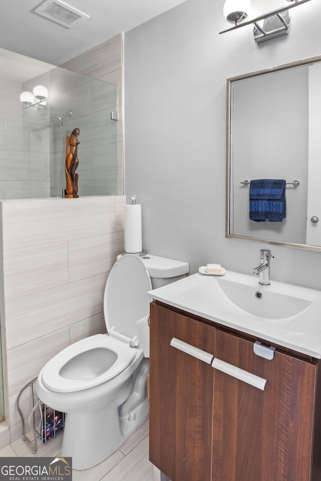 bathroom featuring vanity, toilet, tile walls, and a shower with shower door