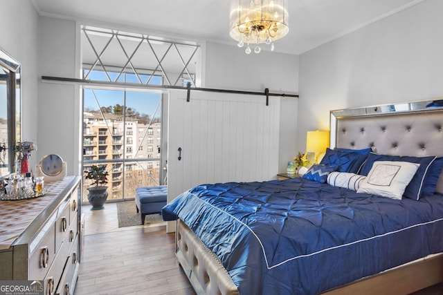 bedroom featuring an inviting chandelier, ornamental molding, a barn door, and light hardwood / wood-style floors