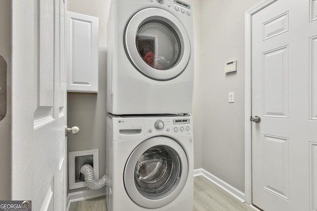 laundry area with cabinets, stacked washing maching and dryer, and light wood-type flooring