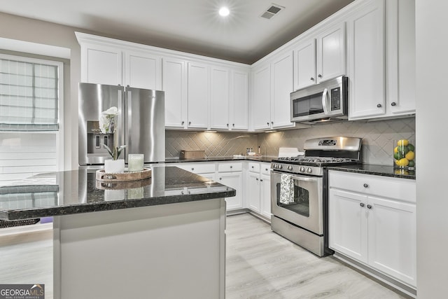 kitchen featuring dark stone countertops, tasteful backsplash, white cabinets, and appliances with stainless steel finishes